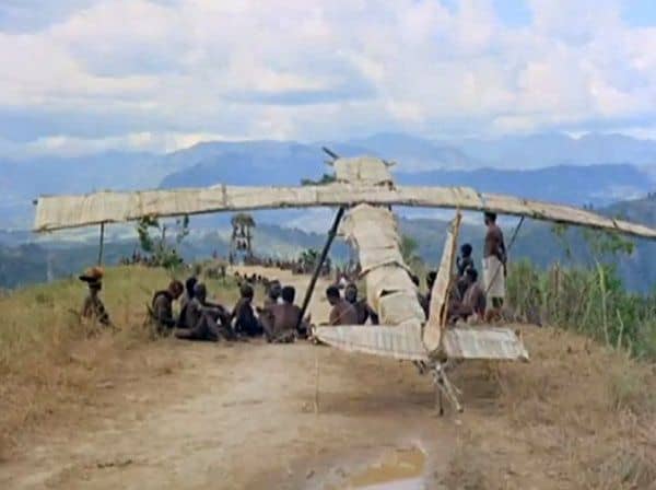 A photo of people sitting in front of a Cargo Cult wooden plane